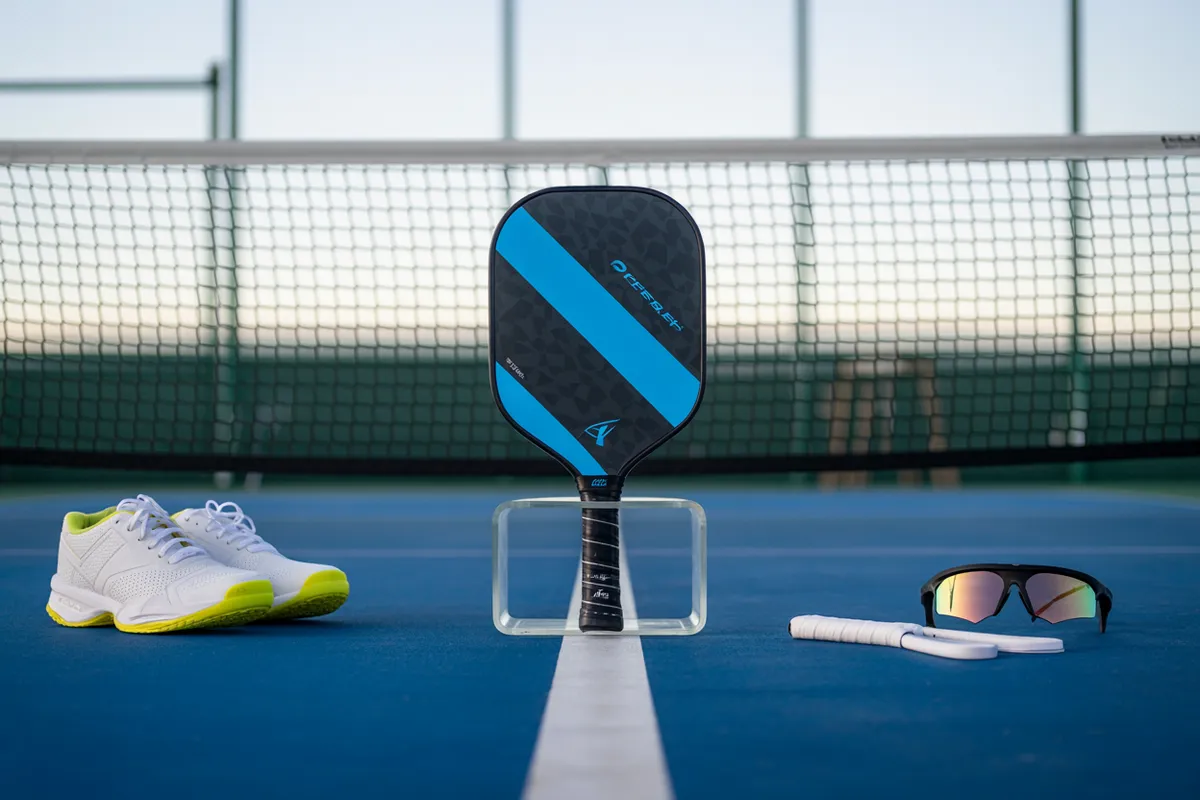 Pickleball gear with a paddle, shoes, and sunglasses on court.