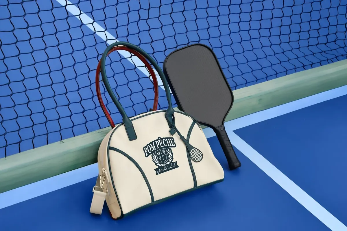 A cream and green sports tote beside a paddle and racket on a blue court.