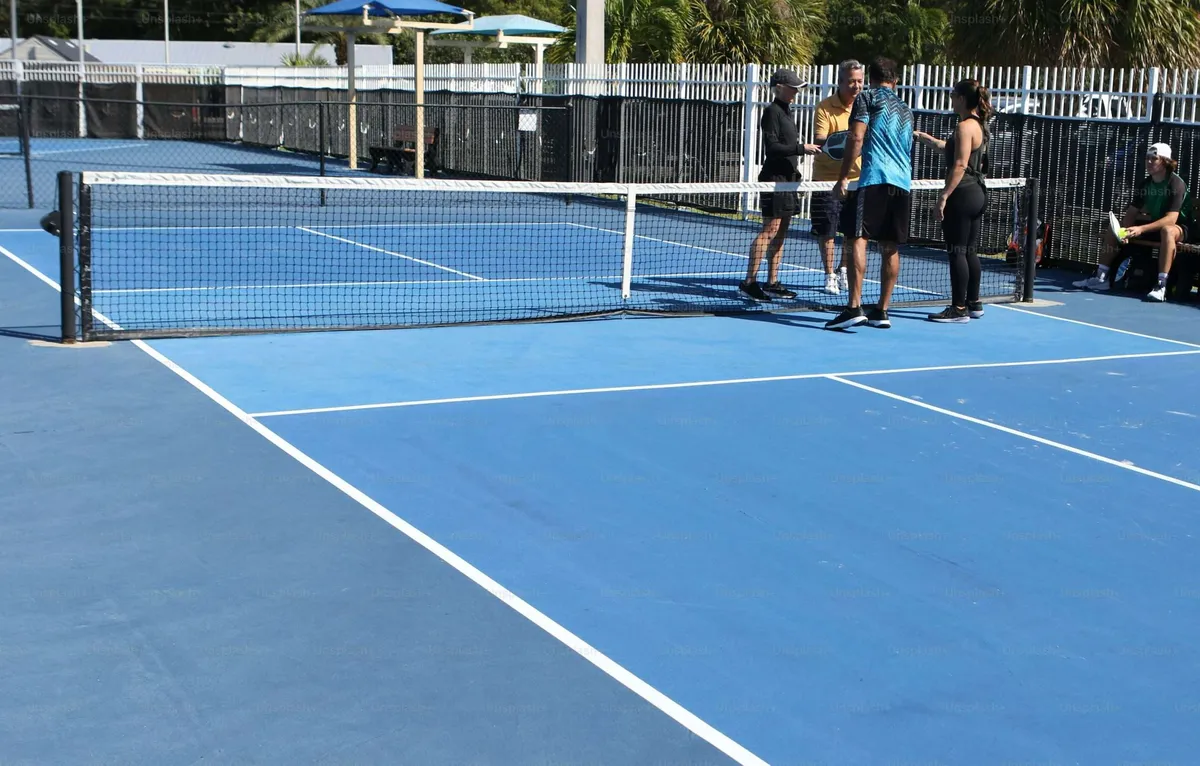 A group of people talking and socializing on a blue pickleball court between games.