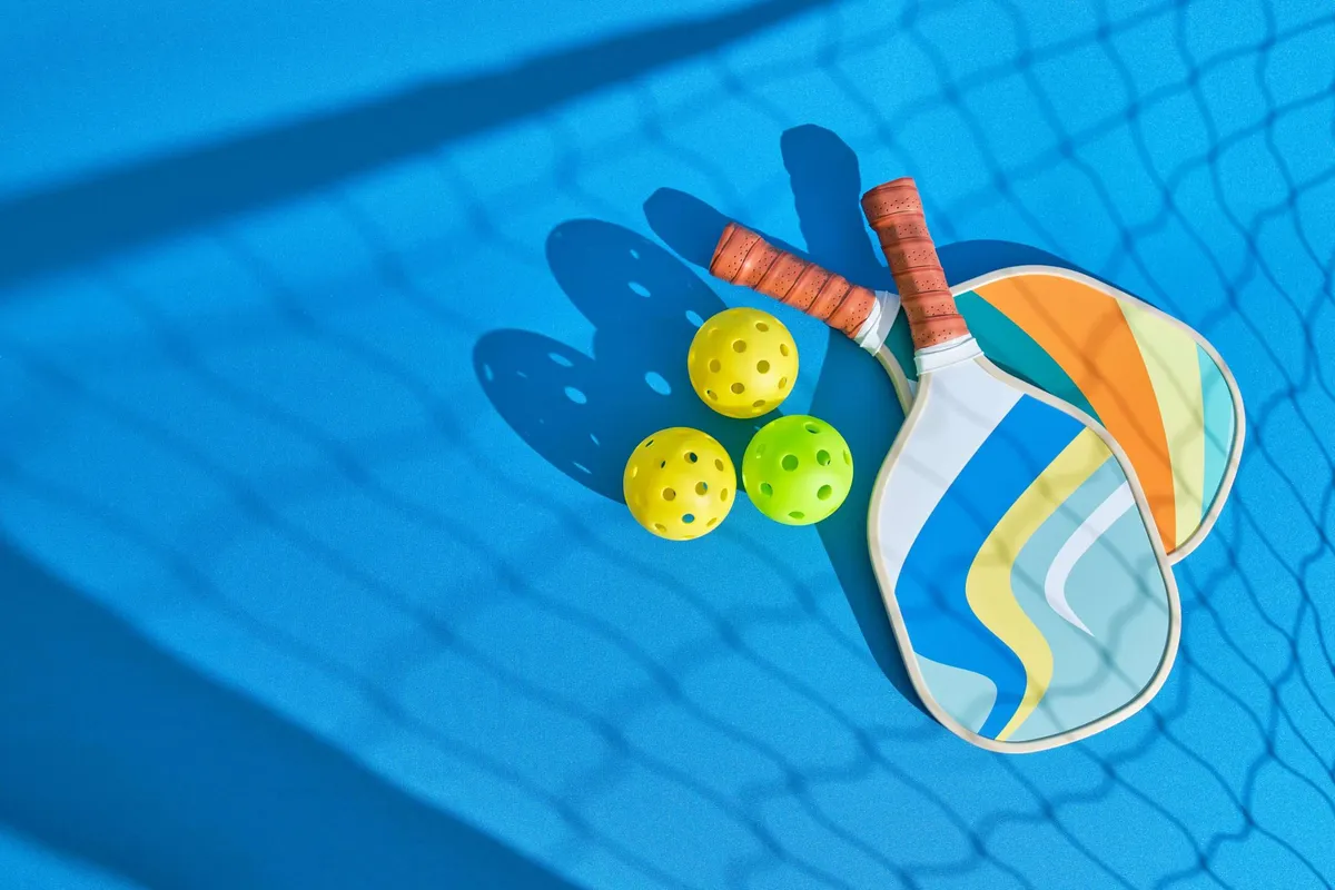 Pickleball paddles and balls on a blue court with net shadow.
