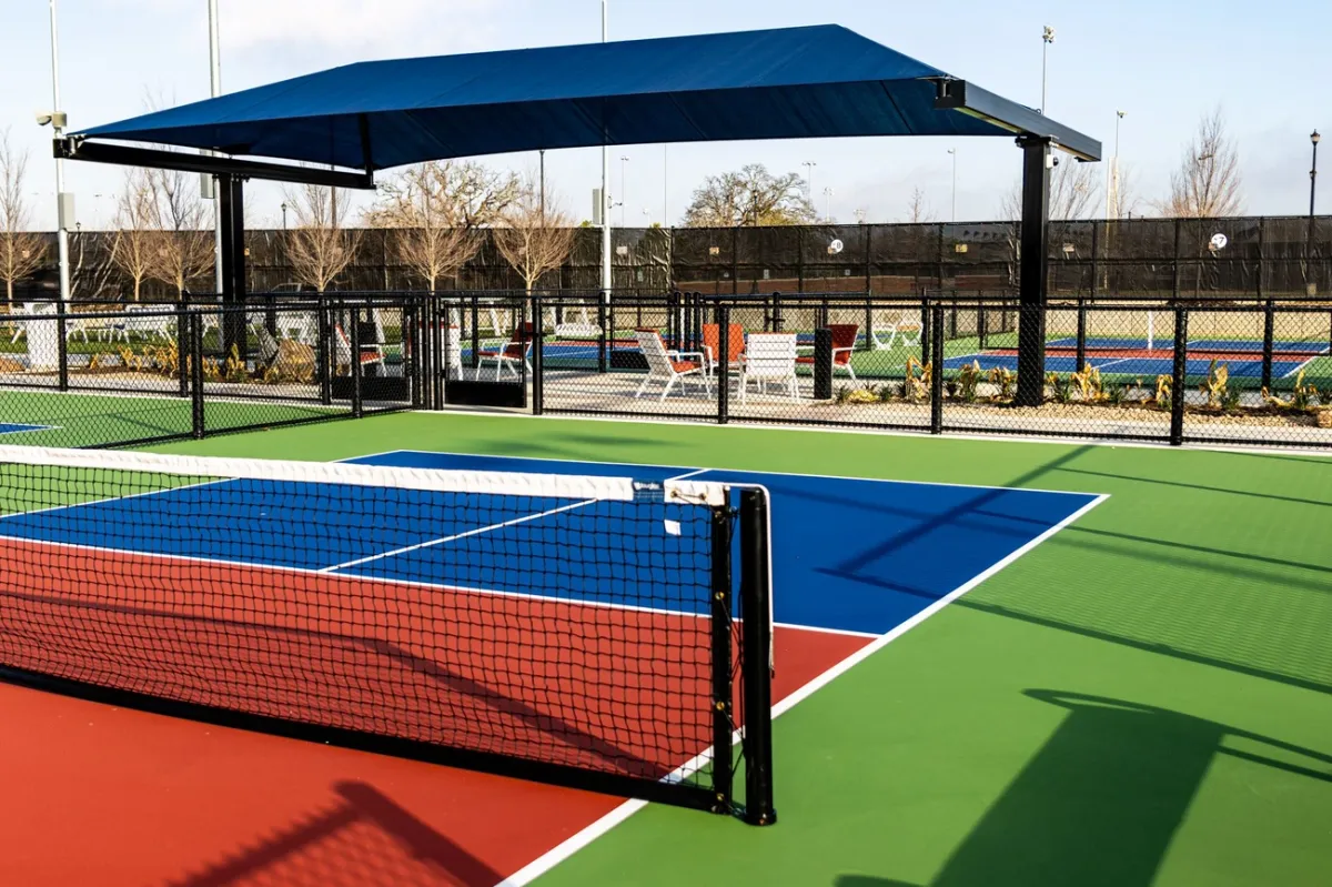 An outdoor pickleball court with a red non-volley zone, blue service area and green surroundings.