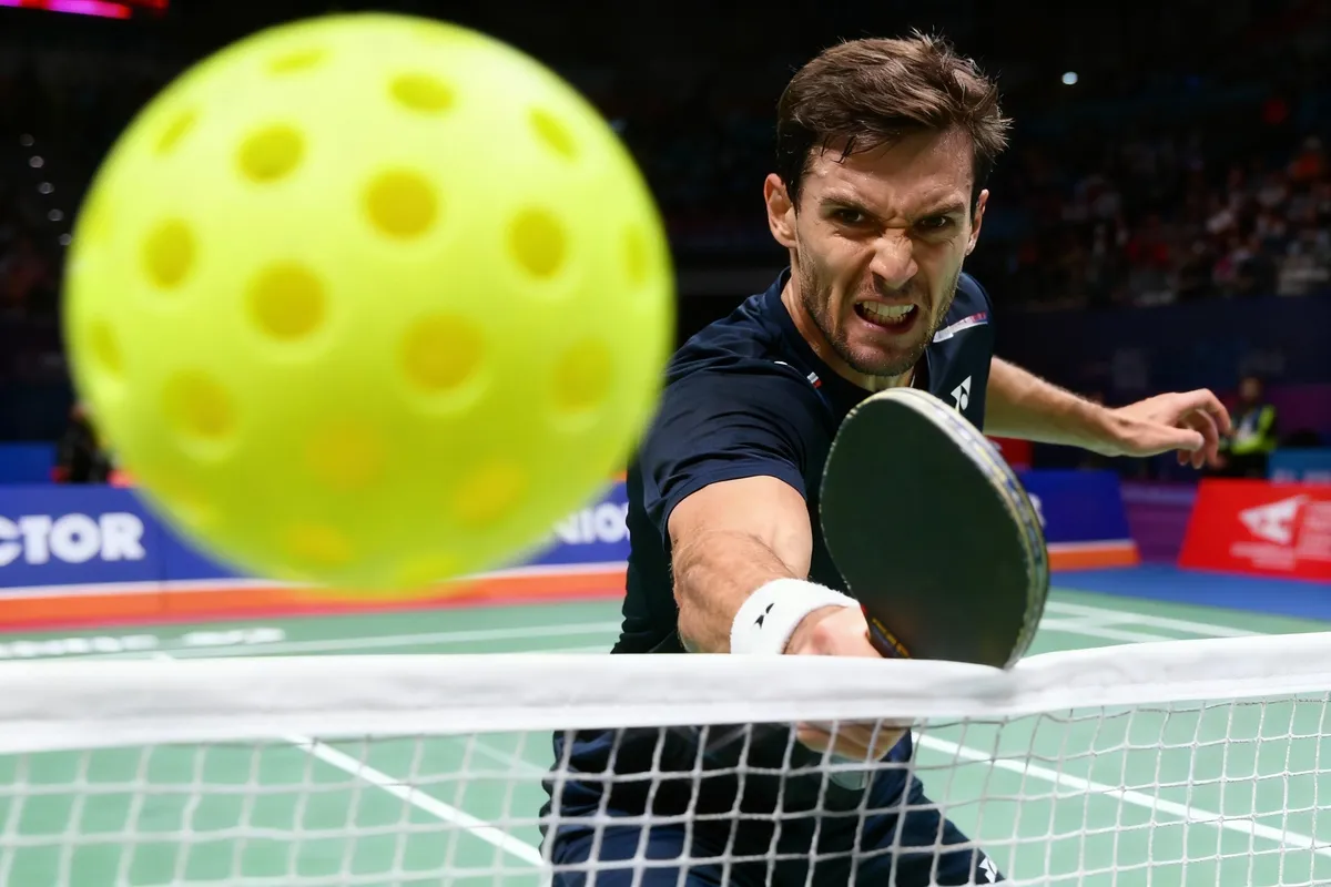 A player extends a paddle toward a yellow ball near the court net.