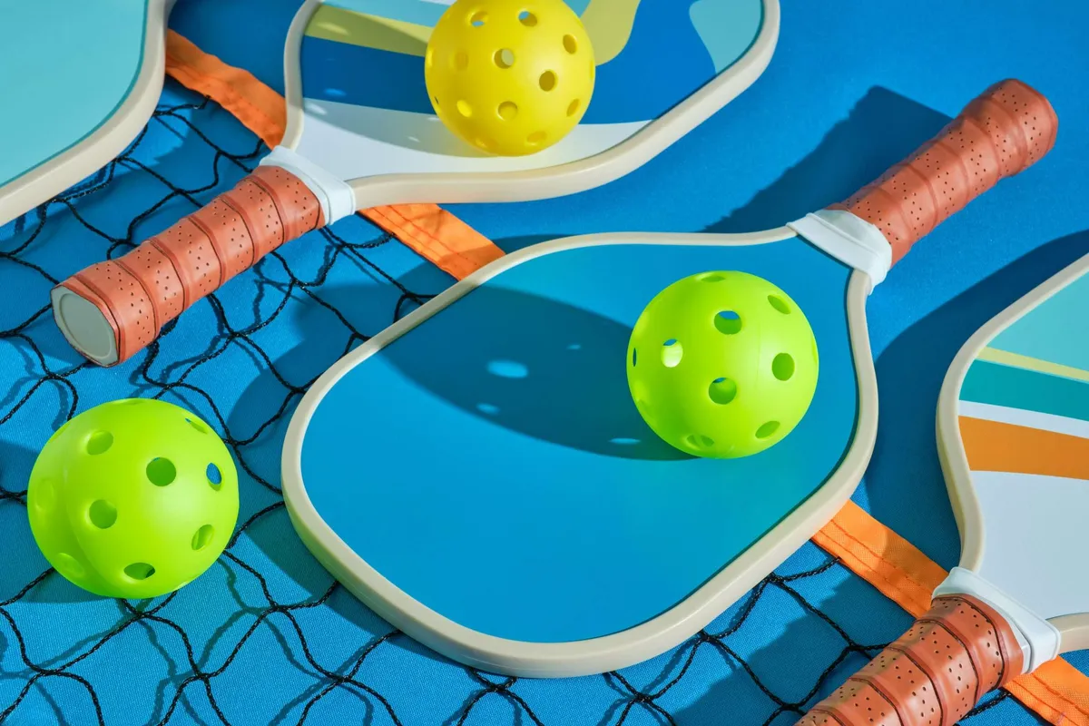 A colorful, flat-lay arrangement of pickleball equipment, including blue paddles with brown grips and bright green and yellow pickleballs.