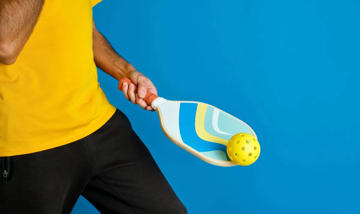 A person in a yellow shirt holding a pickleball and paddle.