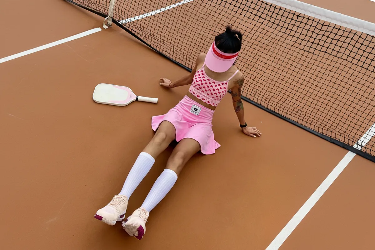 A person in a pink outfit rests against a pickleball net.