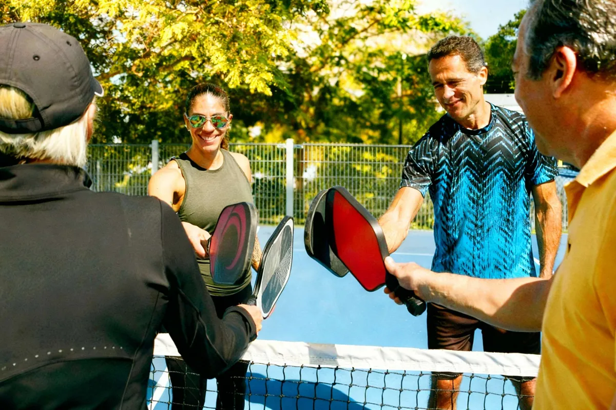 A diverse group of four pickleball players taps paddles over the net after a game
