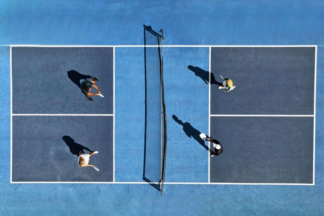 An aerial top-down view of four people playing a doubles match on a blue Pickleball court