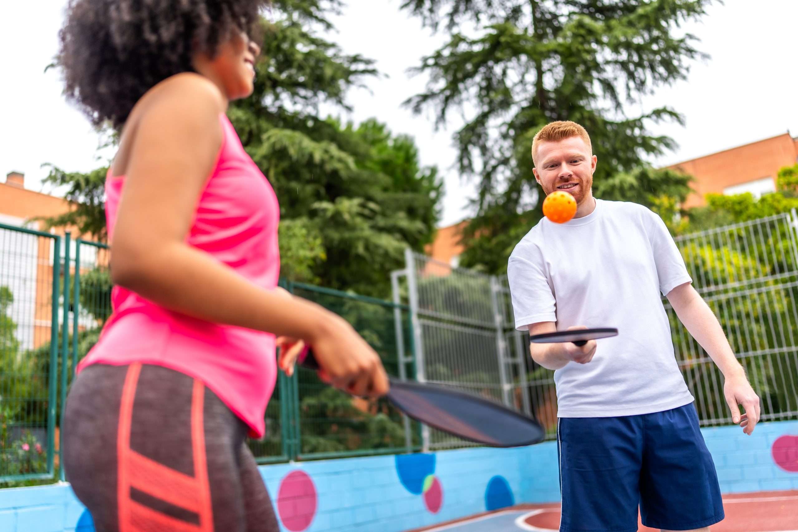 Two teams engaged in a pickleball doubles rally on a sunny outdoor court, showcasing effective court positioning and a fun social sport atmosphere.