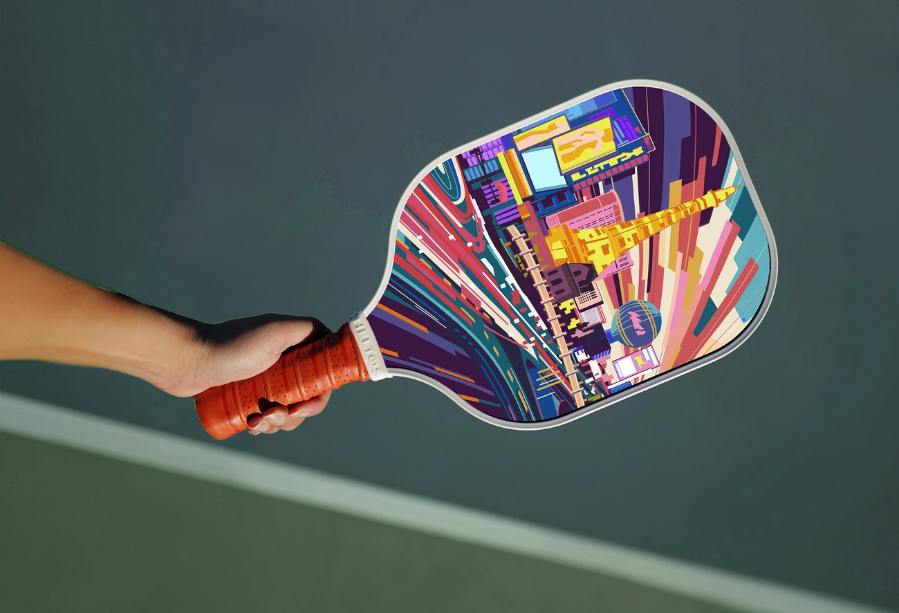 A player holds a custom pickleball paddle featuring a unique paddle graphic of a colorful cityscape, showcasing personal on-court style. 