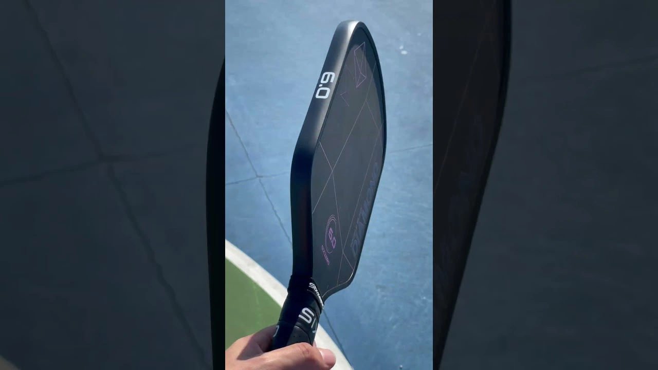 A hand holds a dark paddle with a long face and a short handle.