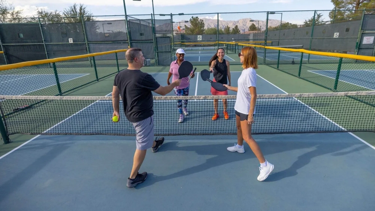 Four players demonstrating good pickleball sportsmanship by tapping paddles over the net at the end of a friendly doubles game. 