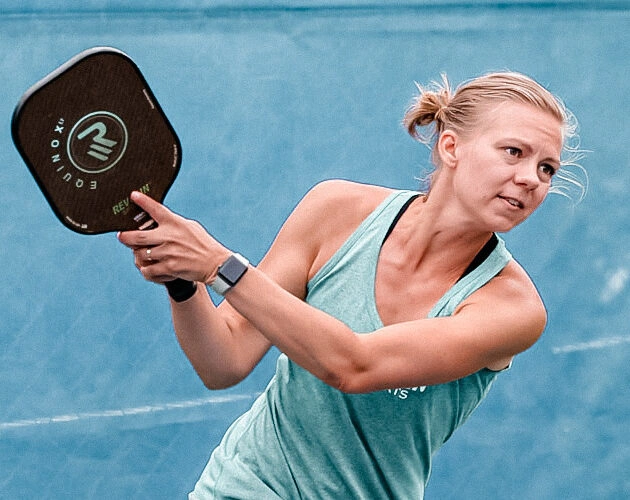 A woman with a focused expression hits a backhand shot during a pickleball game.