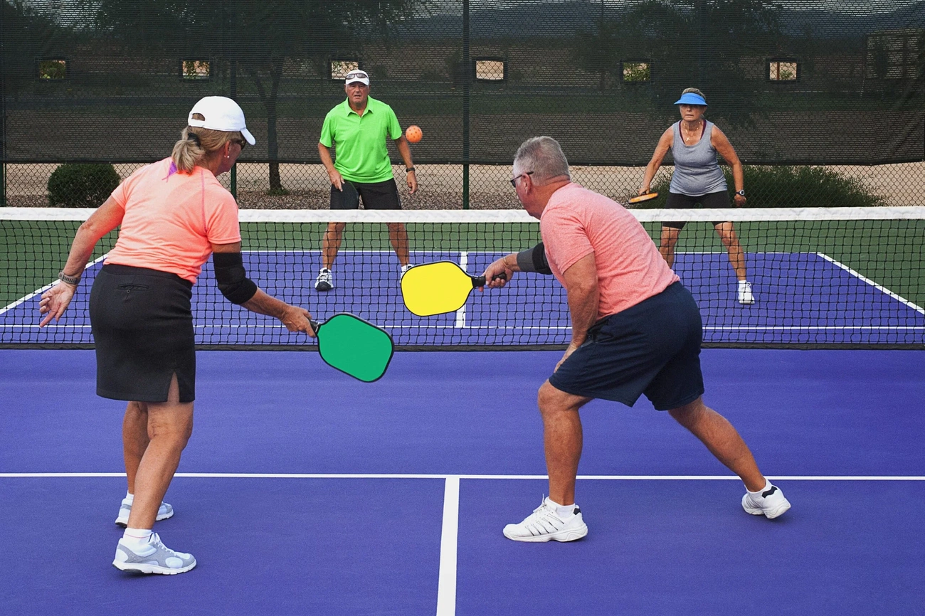 Four seniors engaged in a competitive pickleball mixed doubles match, demonstrating effective court positioning and strategy at the net. 