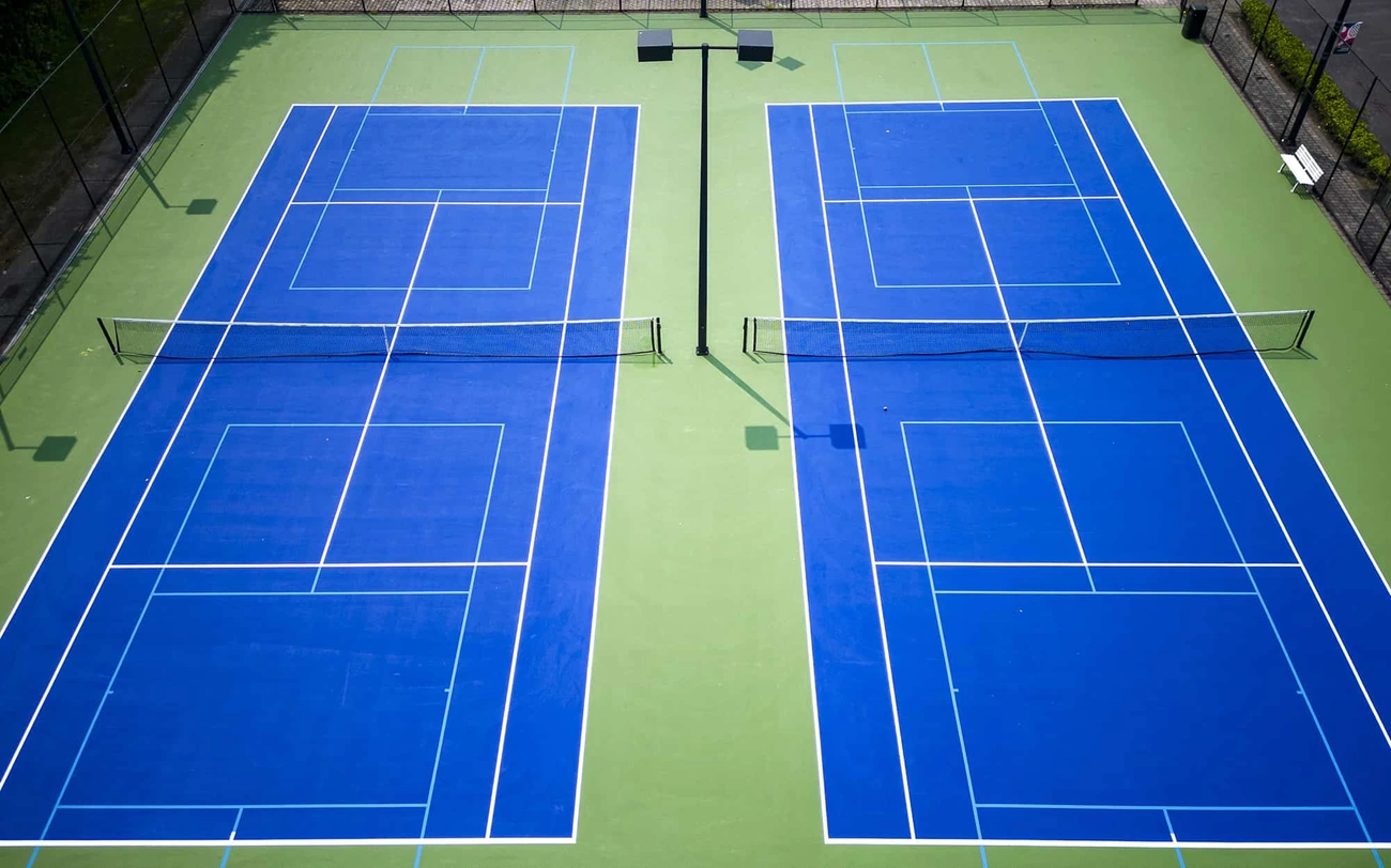 Aerial view of two adjacent blue and green pickleball courts with lighting poles and nets.